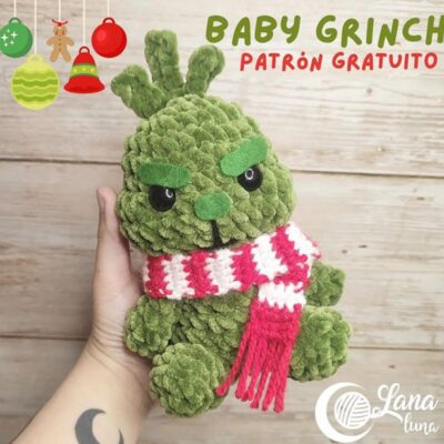 Una mano sostiene un juguete de peluche del Baby Grinch. El juguete está tejido a crochet con hilo verde, tiene una expresión de mal humor con espesas cejas verdes y está envuelto en una bufanda a rayas rojas y blancas. El texto de la imagen dice "Baby Grinch Patrón Gratuito" con decoraciones navideñas.