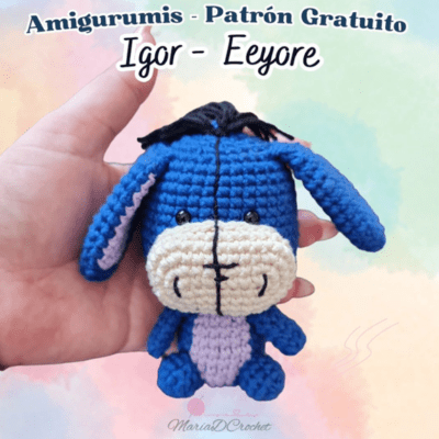 Una persona sostiene un burro azul tejido a crochet con un hocico color crema y un vientre rosado. El fondo es un suave degradado de colores pastel. El texto en la parte superior dice: "Amigurumis - Patrón Gratuito Igor - Eeyore". La parte inferior de la imagen muestra un logotipo. ¡Perfecto para crochet para principiantes!