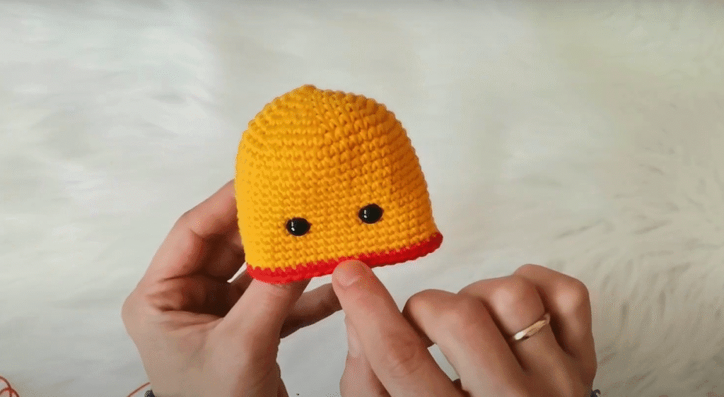 Primer Plano De Una Cabeza De Pollito Amigurumi Tejida a Crochet Con Ala Roja Y Ojos Negros