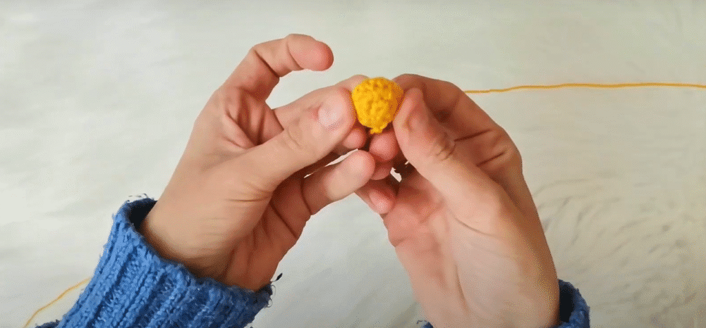Primer Plano De Unas Manos Sosteniendo Una Pequeña Bola Amarilla Tejida a Crochet