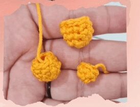 Un Primer Plano De Una Mano Que Sostiene Tres Pequeñas Piezas De Crochet Hechas Con Hilo Amarillo Que Recuerdan Al Amigurumi De Winnie Pooh La Pieza Más Grande Se Asemeja a Una Pequeña Bola Redonda Con Una Cola De Hilo Mientras Que Las Otras Dos Piezas Son Más Pequeñas Y Tienen Formas Diferentes El Fondo Está Ligeramente Borroso