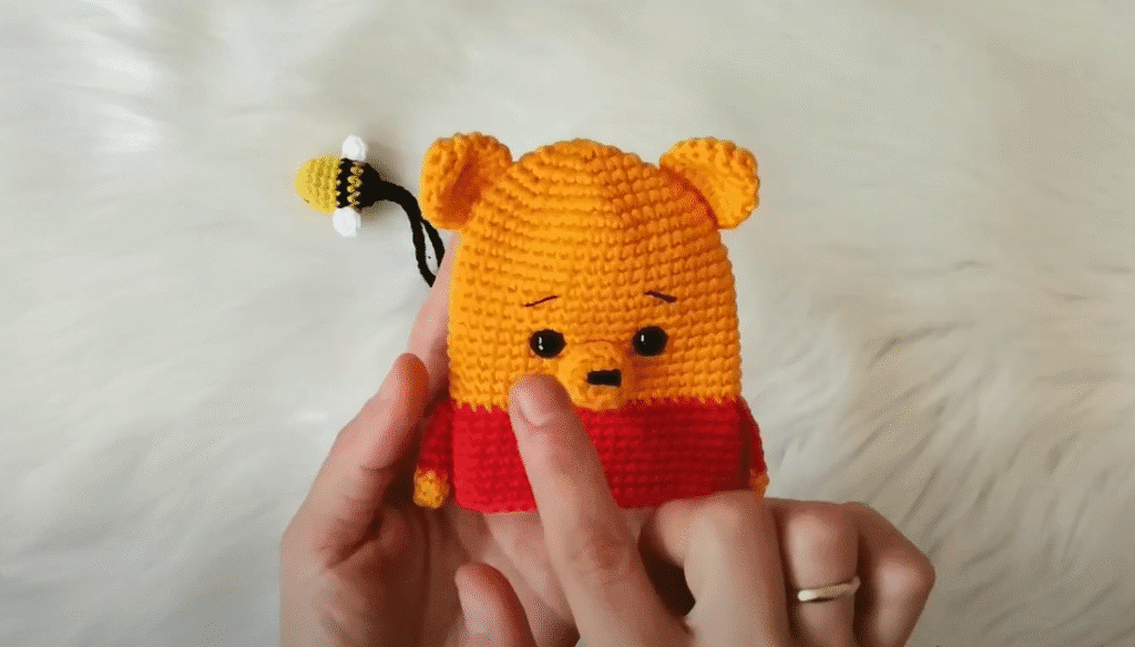 Primer Plano De Unas Manos Sosteniendo Un Llavero Amigurumi De Winnie the Pooh Tejido a Crochet Con Una Abeja