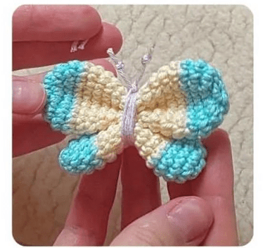 Dos Manos Sostienen Una Pequeña Mariposa Amigurumi Con Alas De Color Azul Claro Y Crema La Mariposa Tiene Una Textura Suave Y Se Muestra Sobre Un Fondo Neutro