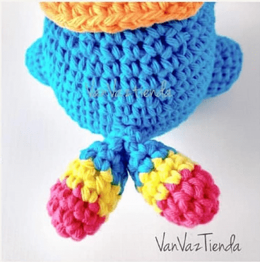 Una Figura Colorida De Crochet Principalmente Azul Con Dos Partes Sobresalientes Que Se Asemejan a Piernas Cada Pata Es Azul En La Parte Superior Con Secciones Alternas De Amarillo Y Rosa En La Parte Inferior En La Figura Y En La Parte Inferior De La Imagen Está Visible El Texto vanvaztiendas Este Adorable Monstruo Colorido Cuenta Con Un Diseño Encantador Perfecto Para Los Amantes De Tejer