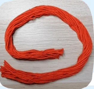 Un Bucle De Hilo De Color Naranja Brillante Se Encuentra Sobre Una Superficie De Madera Clara El Hilo Está Dispuesto De Forma Suelta En Forma Circular Con Algunos Hilos Retorcidos En La Parte Inferior Izquierda