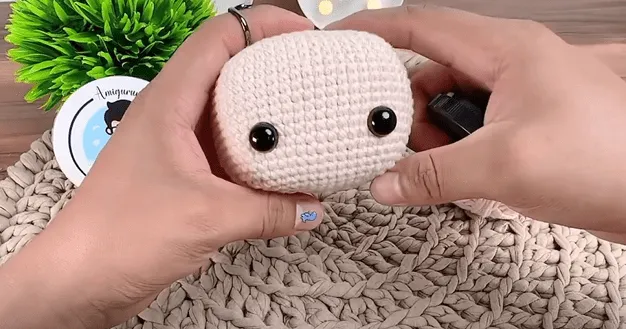 Primer plano de unas manos uniendo los ojos a una cabeza de amigurumi tejida a crochet.