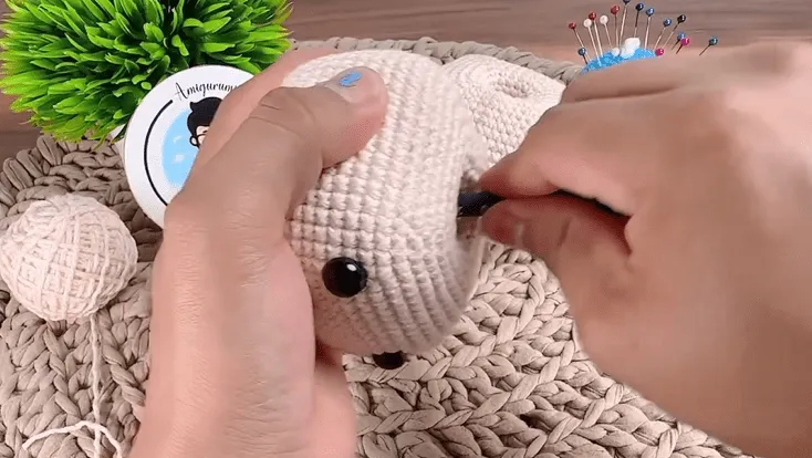 Primer plano de manos tejiendo a crochet la cara del animal amigurumi, añadiendo detalles.