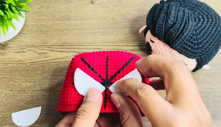 Primer plano de manos uniendo ojos de fieltro a un amigurumi de Spiderman tejido a crochet.