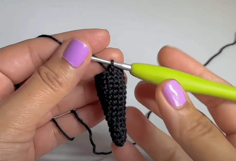 Primer plano de manos tejiendo un cono de amigurumi negro.