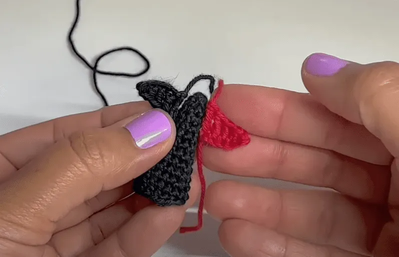 Primer plano de manos tejiendo un pequeño pingüino amigurumi, colocando un detalle rojo.