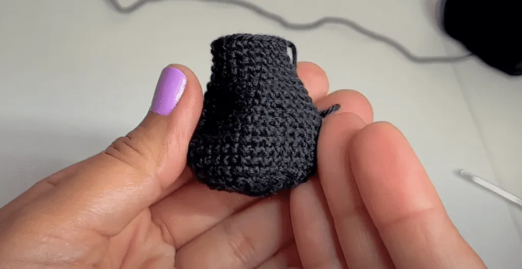 Primer plano de unas manos sosteniendo un pequeño amigurumi de color gris oscuro tejido a crochet.