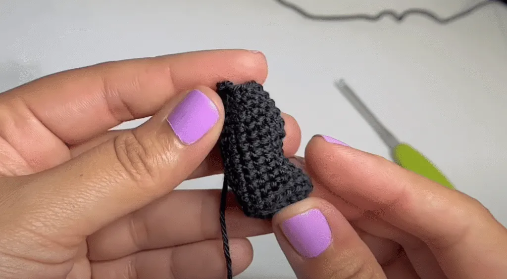 Primer plano de unas manos tejiendo a crochet una pequeña pieza de amigurumi de color gris oscuro.