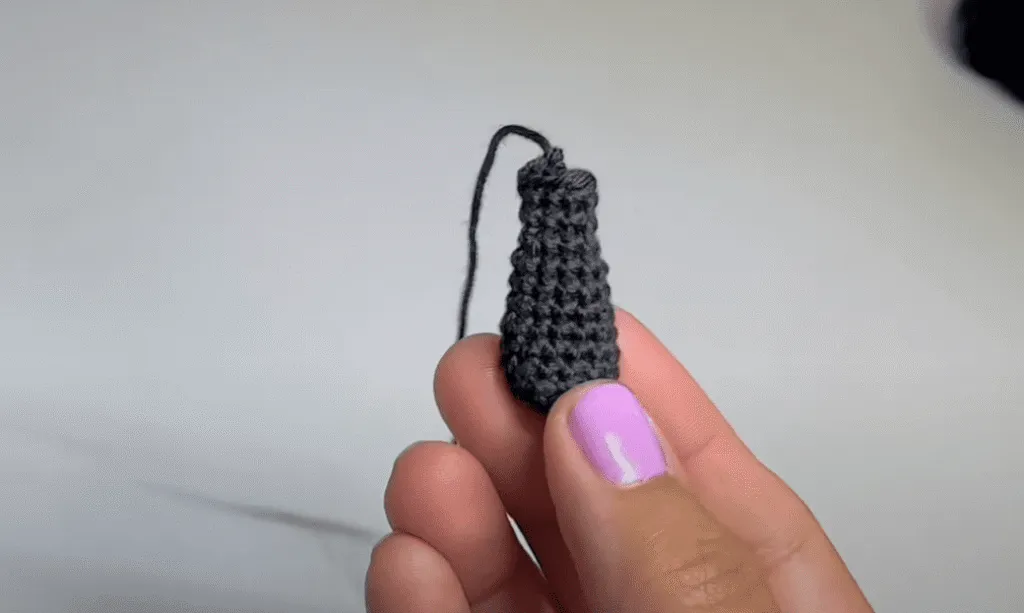 Primer plano de una mano sosteniendo un pequeño cono de ganchillo de color gris oscuro.
