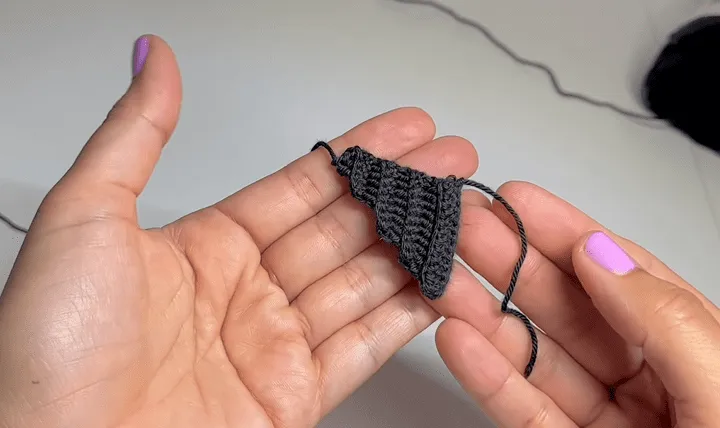 Primer plano de unas manos sosteniendo un pequeño triángulo negro tejido a crochet.