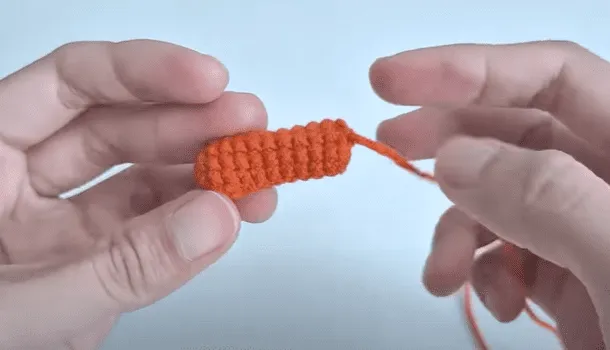 Primer plano de unas manos sosteniendo una pequeña pieza de crochet de color naranja.