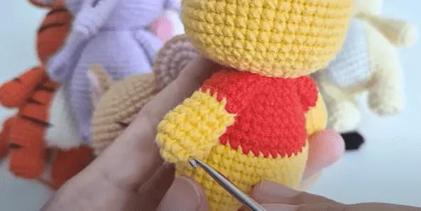 Primer plano del amigurumi de Winnie the Pooh tejido a crochet, mostrando detalles del cuerpo amarillo y la camisa roja.