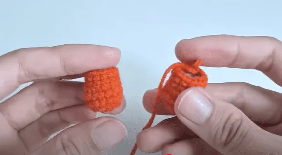 Primer plano de dos pequeñas piezas de color naranja tejidas a crochet, una de ellas con un extremo suelto.