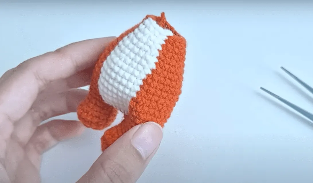 Juguete de panda amigurumi tejido a crochet, parcialmente completo, mostrando secciones naranjas y blancas.