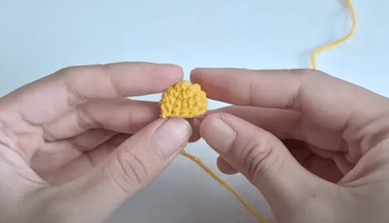 Primer plano de unas manos sosteniendo una pequeña pieza amarilla tejida a crochet.