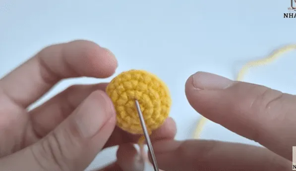 Primer plano de manos tejiendo un círculo amigurumi amarillo.