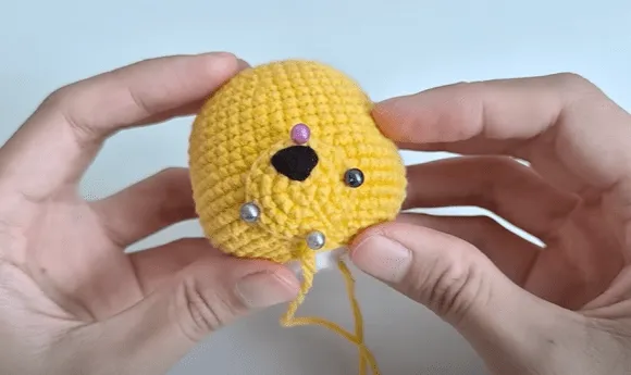 Primer plano de unas manos sosteniendo un pollito amarillo tejido a crochet con características añadidas