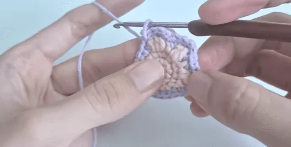 Primer plano de manos tejiendo un cuadrado granny morado y rosa.