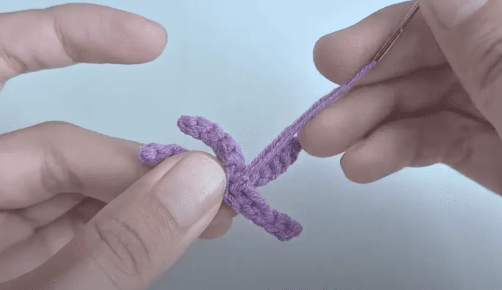 Primer plano de manos tejiendo una pieza de amigurumi de color morado.