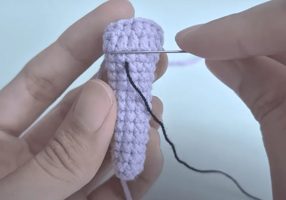 Primer plano de manos bordando hilo negro sobre una pieza de crochet de color morado.