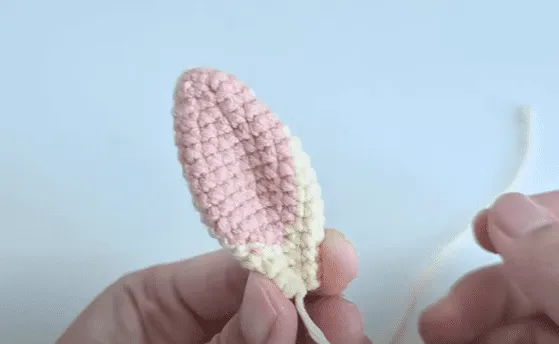 Primer plano de una oreja de conejo tejida a crochet, mitad rosa y mitad crema.