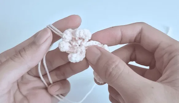 Primer plano de manos tejiendo a crochet una delicada flor de color crema.