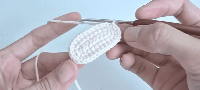 Primer plano de manos tejiendo a crochet una pequeña pieza de forma ovalada.