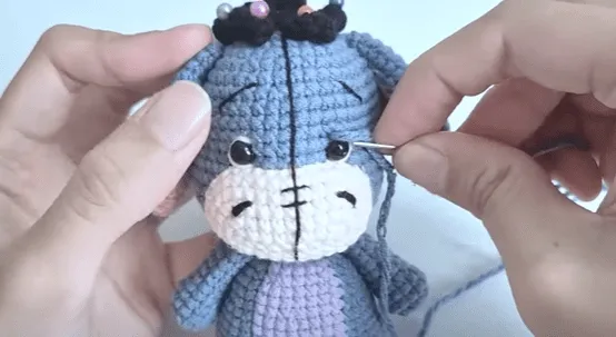 Primer plano de manos tejiendo el ojo de Eeyore en un amigurumi.
