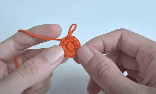 Primer plano de unas manos sosteniendo un pequeño círculo naranja tejido a crochet.