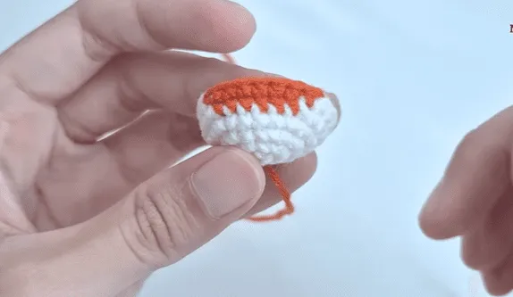 Primer plano de unas manos sosteniendo un pequeño amigurumi de crochet, mitad naranja y mitad blanco.
