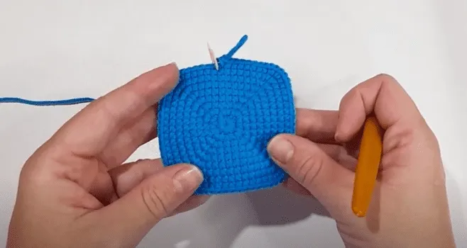 Primer plano de manos tejiendo un cuadrado azul brillante.