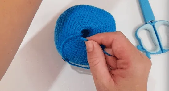 Primer plano de unas manos tirando de una cola de hilo a través de un círculo tejido a crochet.