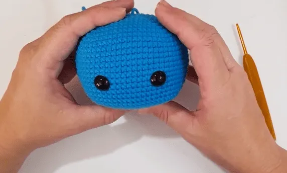Primer plano de un juguete amigurumi azul tejido a crochet con ojos de seguridad negros.