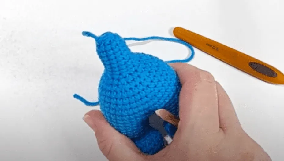 Primer plano de manos tejiendo a crochet el cuerpo de un elefante amigurumi azul.