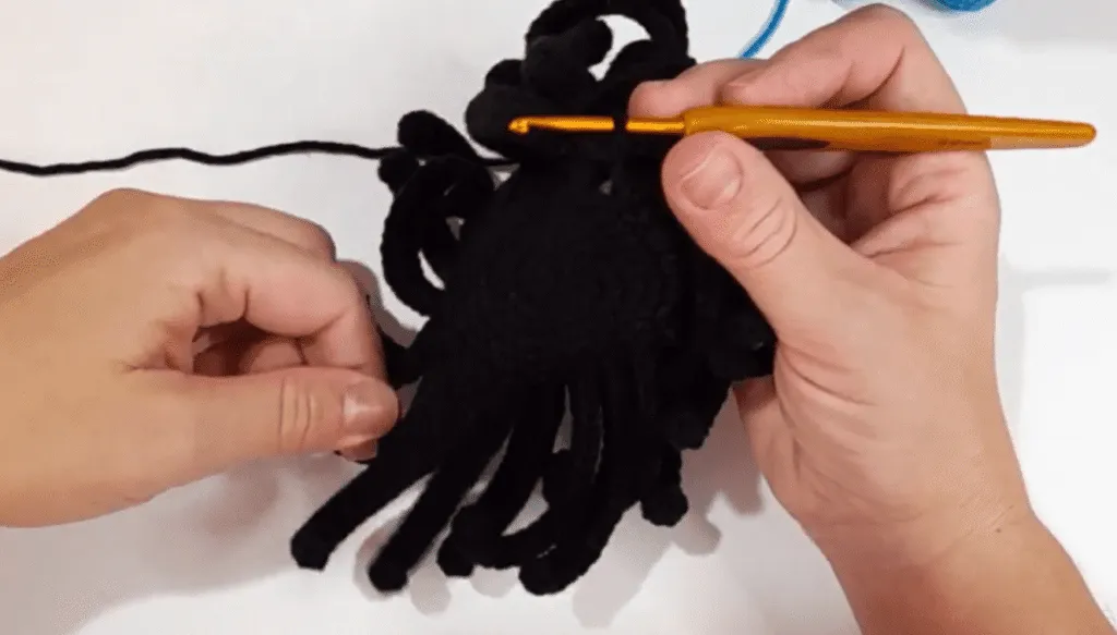 Primer plano de manos tejiendo a crochet una araña amigurumi negra.