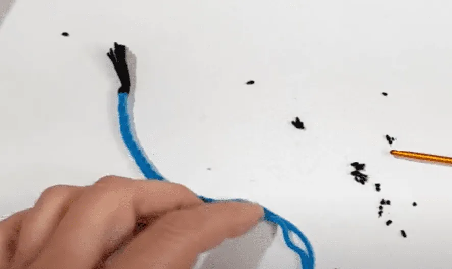 Primer plano de unas manos sosteniendo un hilo trenzado de color turquesa y negro.