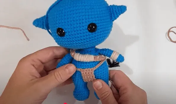 Primer plano de unas manos sosteniendo un juguete amigurumi tejido a crochet, con cuerpo azul y detalles en color canela.