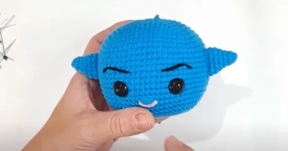 Primer plano de un juguete amigurumi tejido a crochet con cuernos, que se asemeja a un simpático personaje de dibujos animados.