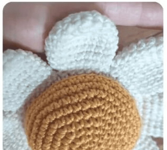 Vista Cercana De Una Flor Tejida a Crochet Perfecta Para Un Alfiletero De Margarita La Flor Tiene Un Centro Redondo Texturizado Marrón Y Varios Pétalos Blancos Al Fondo Se Ve Parcialmente Una Mano Que Sostiene La Flor La Imagen Resalta Los Intrincados Detalles Y La Artesanía Del Trabajo De Crochet