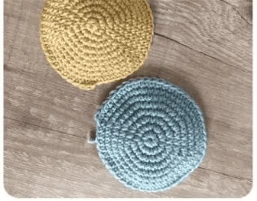 Sobre Una Superficie De Madera Se Exponen Dos Posavasos Redondos Tejidos a Mano El Posavasos De Arriba Es De Color Amarillo Mostaza Y El De Abajo Es De Color Azul Claro La Textura De Ambos Posavasos Presenta Un Patrón En Espiral Indicativo Del Trabajo De Crochet Perfecto Para Agregar Un Toque De Encanto a Tu Colección De Manualidades En Tela