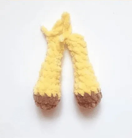 Primer plano de dos patas de jirafa tejidas a crochet, de color amarillo y con pezuñas marrones.