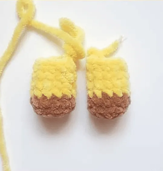 Adorables botitas de bebé hechas a mano, de color amarillo y marrón, unidas mediante lazos de hilo.