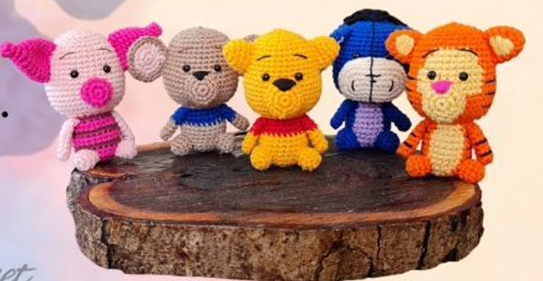 Un Grupo De Cinco Animales De Peluche Tejidos a Crochet Entre Ellos Un Cerdo Rosa Un Burro Gris Un Oso Amarillo Un Burro Azul Llamado Pequeño Igor Y Un Tigre Naranja Están Dispuestos Sobre Una Losa De Madera Cada Personaje Está Detallado Con Distintos Colores Y Características Mostrando Un Intrincado Trabajo De Crochet Perfecto Para Crochet Para Principiantes