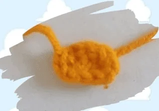 Un Pequeño Objeto De Ganchillo De Color Amarillo Brillante Que Se Asemeja a Un Animal Abstracto Posiblemente Con Cola Colocado Sobre Un Fondo Azul Claro Con Nubes Blancas