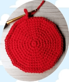 Un Primer Plano De Un Círculo Rojo Tejido a Crochet En Progreso Apoyado Sobre Una Superficie De Madera Se Coloca Un Ganchillo Dorado Con Un Mango Negro En La Parte Superior Del Círculo Y Se Enrolla Un Hilo De Hilo Rojo En El Ganchillo El Fondo Presenta Nubes Blancas Sobre Un Cielo Azul