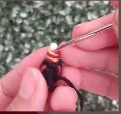 Una Persona Está Usando Una Herramienta Para Derretir Y Dar Forma Al Extremo De Una Pulsera De Paracord Multicolor Sobre Un Fondo Verde Borroso El Paracord Que Recuerda Los Tonos Vibrantes Del Amigurumi Alicia En El País De Las Maravillas Presenta Segmentos De Amarillo Rojo Y Negro